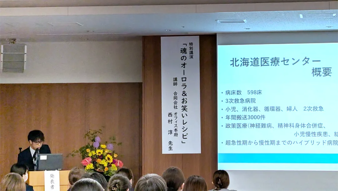 北海道医療センター概要のスライド(病床数598床、3次救急病院など)を背景に発表を行う様子
